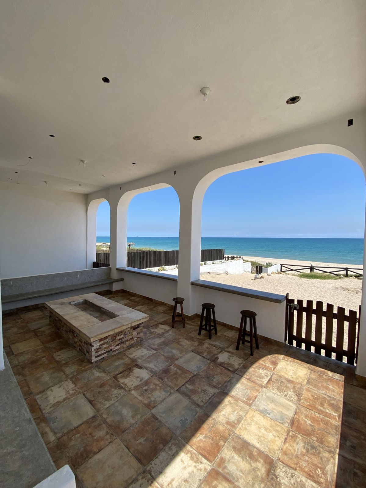 Terraza techada con fogatero y arcos abiertos hacia la playa